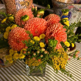 Coral dahlias and yellow filler flowers in a clear glass vase