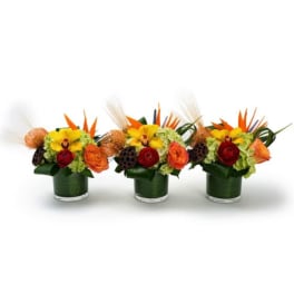 Trio of low orange, red, and yellow floral centerpieces in clear glass vases