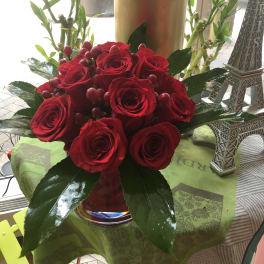 Red roses arranged in a glass vase with glossy leaves