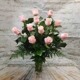 Pink roses arranged in a clear glass vase with fern foliage