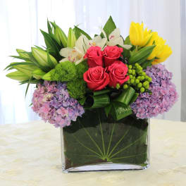 Mixed bouquet in a clear square vase with roses, lilies, hydrangeas, and tulips