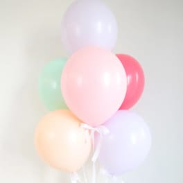 Pastel balloons tied together with a white ribbon against a plain wall.