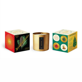 Gold candle in a metal tin between two decorative product boxes