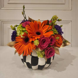 Orange gerbera daisies and pink roses in a black-and-white pumpkin vase