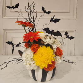 Halloween floral arrangement in a striped pumpkin container with bat picks