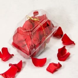 Clear gift box filled with red rose petals and tied with a gold ribbon