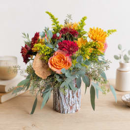 Mixed bouquet with orange and burgundy flowers in a bark-covered vase