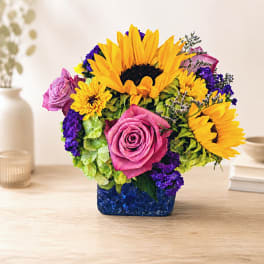 Colorful bouquet with sunflowers, pink roses, and purple flowers in a blue vase