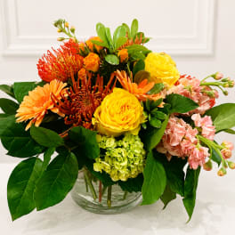 Mixed bouquet of yellow, orange, pink, and red flowers in a glass vase
