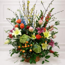 Large mixed flower arrangement in a wicker basket with lilies, roses, and branches