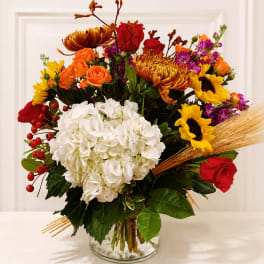 Mixed bouquet with white hydrangea, red roses, sunflowers, and orange blooms in a glass vase