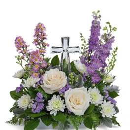 White roses and purple flowers arranged around a clear glass cross