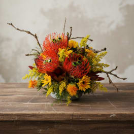 Bright orange and yellow floral arrangement with branch accents in a low bowl