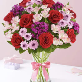 Bouquet of red roses and pink flowers in a glass vase with a pink ribbon