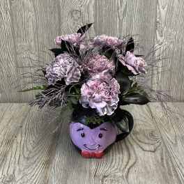 Pink carnations arranged in a purple face mug with a red bow