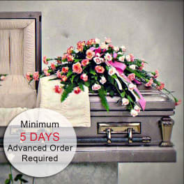 Pink and peach rose casket spray with ribbon displayed on a silver casket