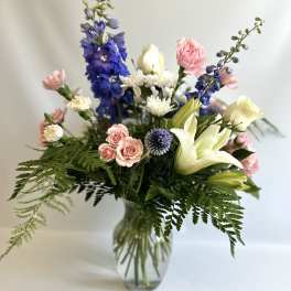 Mixed bouquet of pink, white, and blue flowers in a glass vase