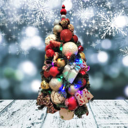 Tabletop Christmas tree with red and gold ornaments, gift boxes, and lights in a small pot