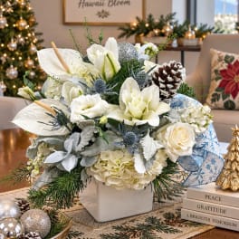 White floral arrangement in a square vase with pinecones and winter accents