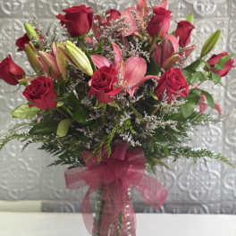 Bouquet of red roses and pink lilies in a clear glass vase with a pink ribbon