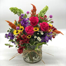 Mixed bouquet of pink roses, purple flowers, and sunflowers in a glass vase