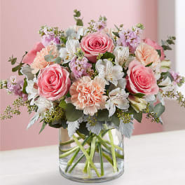 Pink roses and peach flowers arranged in a clear glass vase