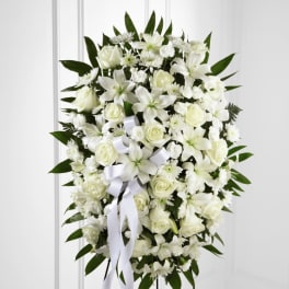 Oval white standing spray with lilies, roses, and carnations on an easel stand.