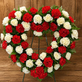 Heart-shaped wreath of red and white carnations on a metal stand