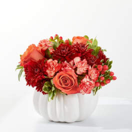 Orange roses and red flowers arranged in a white pumpkin vase