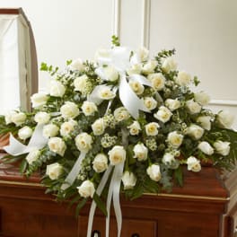 White rose casket spray with ribbon on a wooden casket