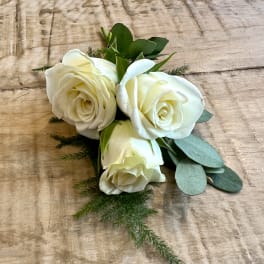 Three white roses with greenery on a wooden surface