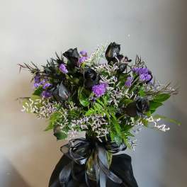 Black roses and purple filler flowers in a glass vase with a black ribbon