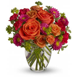 Orange roses and magenta daisies in a clear glass vase