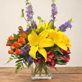 Colorful bouquet with yellow lilies, orange roses, and purple flowers in a clear vase