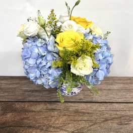 Blue hydrangeas with yellow and white roses in a small vase