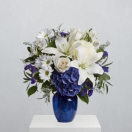 White lilies, blue hydrangea, and daisies arranged in a blue vase