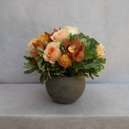 Peach roses and orange orchids arranged in a round gray vase
