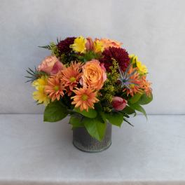 Mixed bouquet of orange, yellow, and burgundy flowers in a metal vase