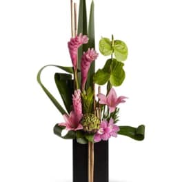 Pink tropical flowers in a black vase with tall leaves and bamboo accents
