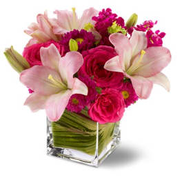 Pink lilies and roses arranged in a clear square vase