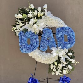 Floral standing tribute spelling DAD with blue and white flowers