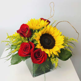 Red roses and yellow sunflowers in a square glass vase
