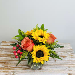 Sunflowers and orange roses in a clear glass vase