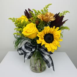 Yellow roses and sunflowers in a glass jar with a black-and-white ribbon