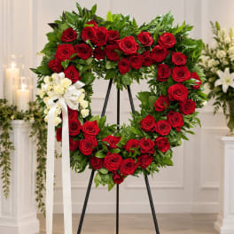 Heart-shaped wreath of red roses with a white ribbon bow on an easel
