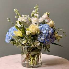 Blue hydrangeas and pale roses arranged in a clear glass vase
