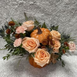 Peach roses and pink carnations arranged around a small pumpkin centerpiece