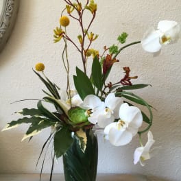 White orchids and yellow accent flowers in a glass vase