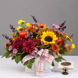 Autumn flower arrangement in a white basket with a plaid ribbon and small pumpkins