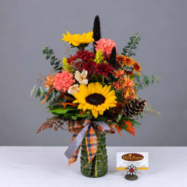 Mixed autumn bouquet in a green glass vase with a plaid ribbon